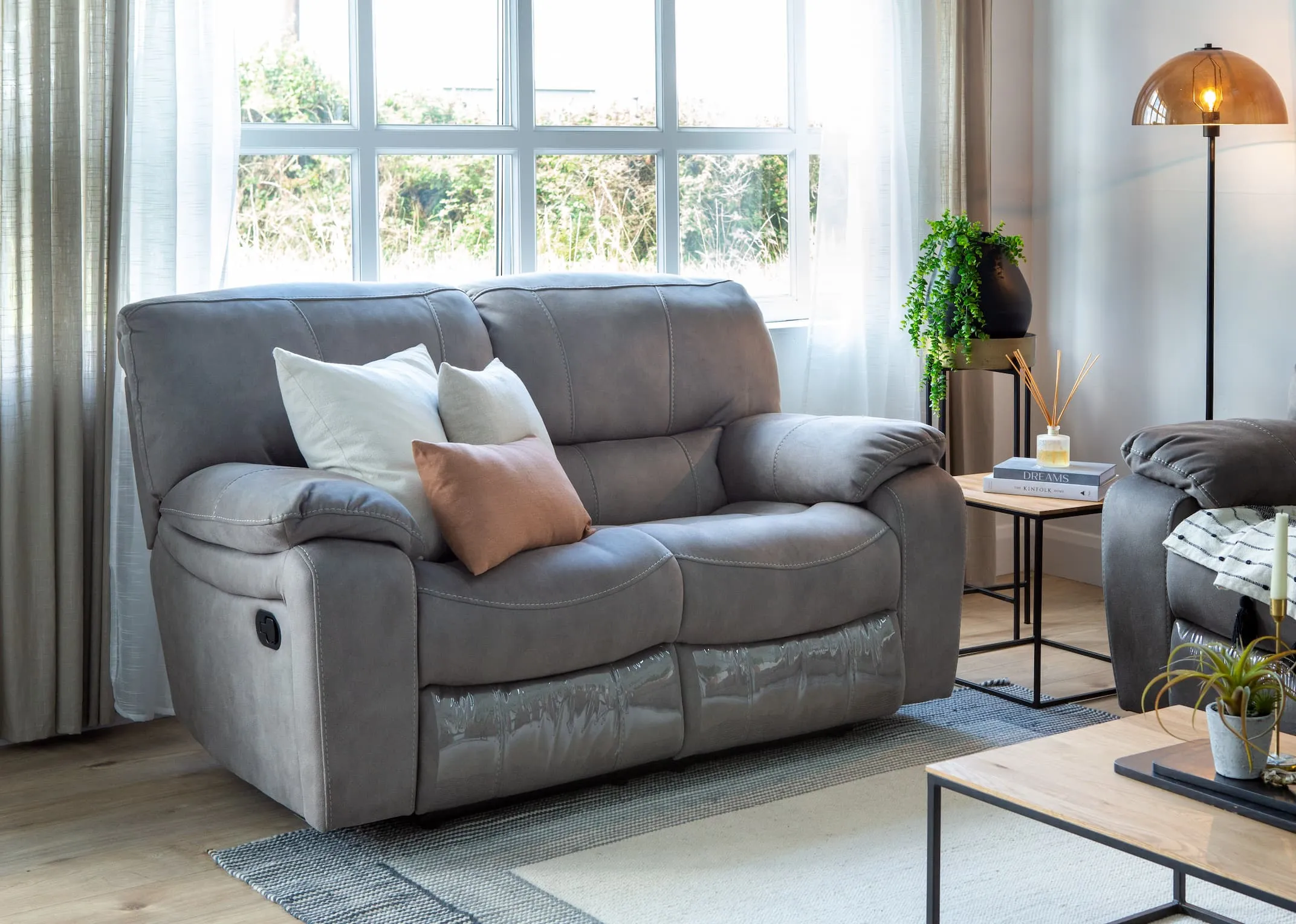A lifestyle image of the Bradford grey 2 seater sofa in fixed mode with the Aston tables & Mellan floor lamp.
