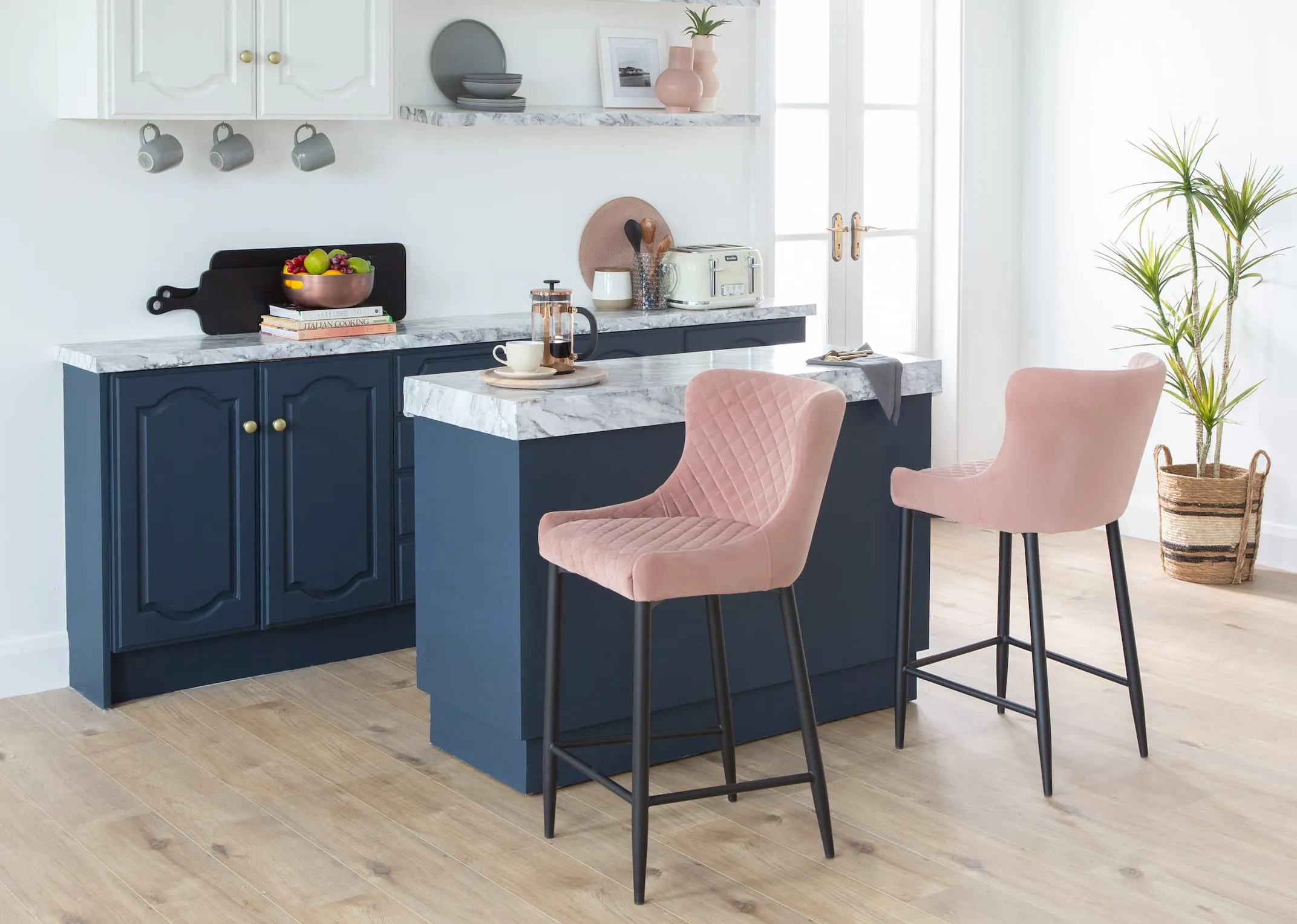 A lifestyle image of the Ottowa bar stools in pink at a navy kitchen island