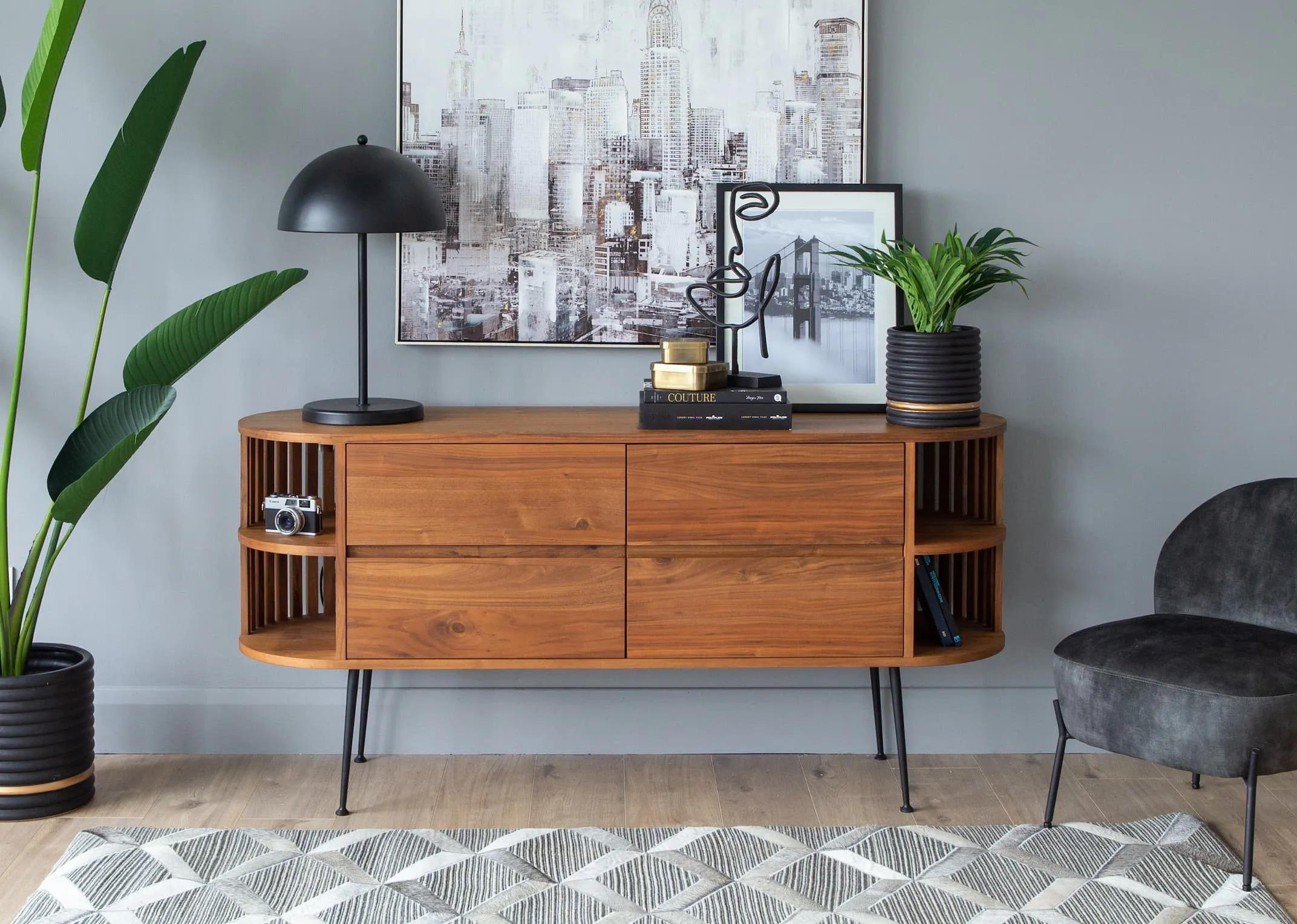 A lifestyle image of the recap sideboard with sarsfield lamp and cityscape print with Palm tree pot