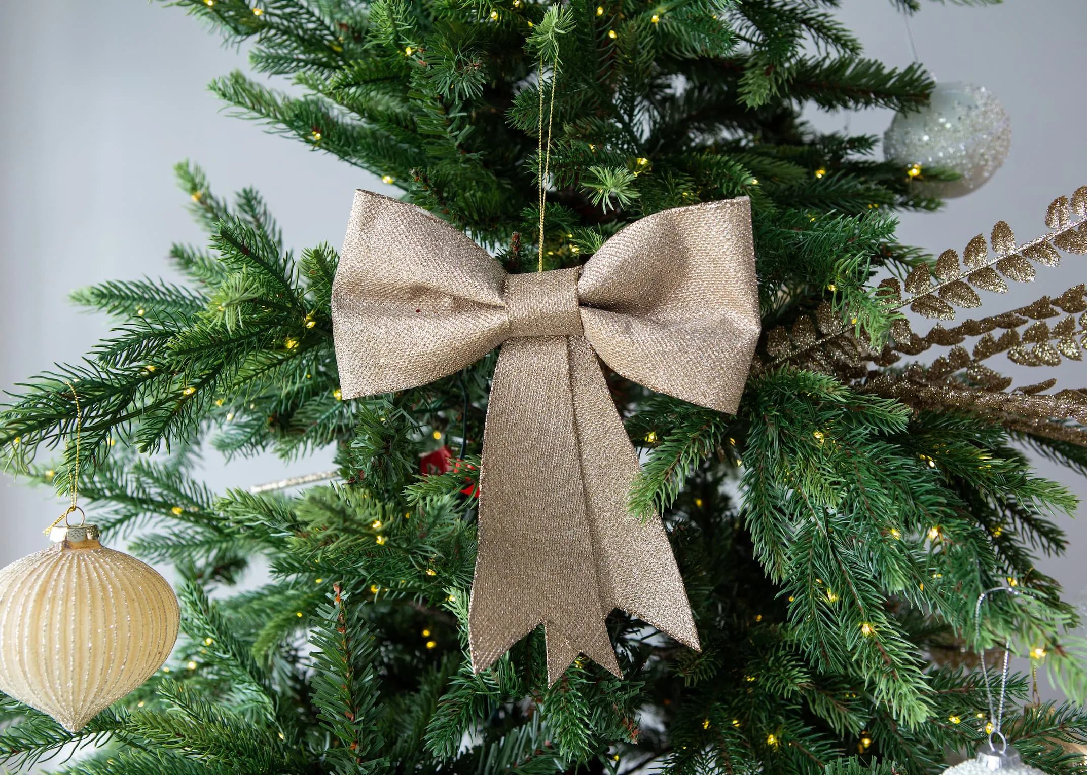 A lifestyle image of the small gold decorative bow decoration on an EZ Living furniture christmas tree.
