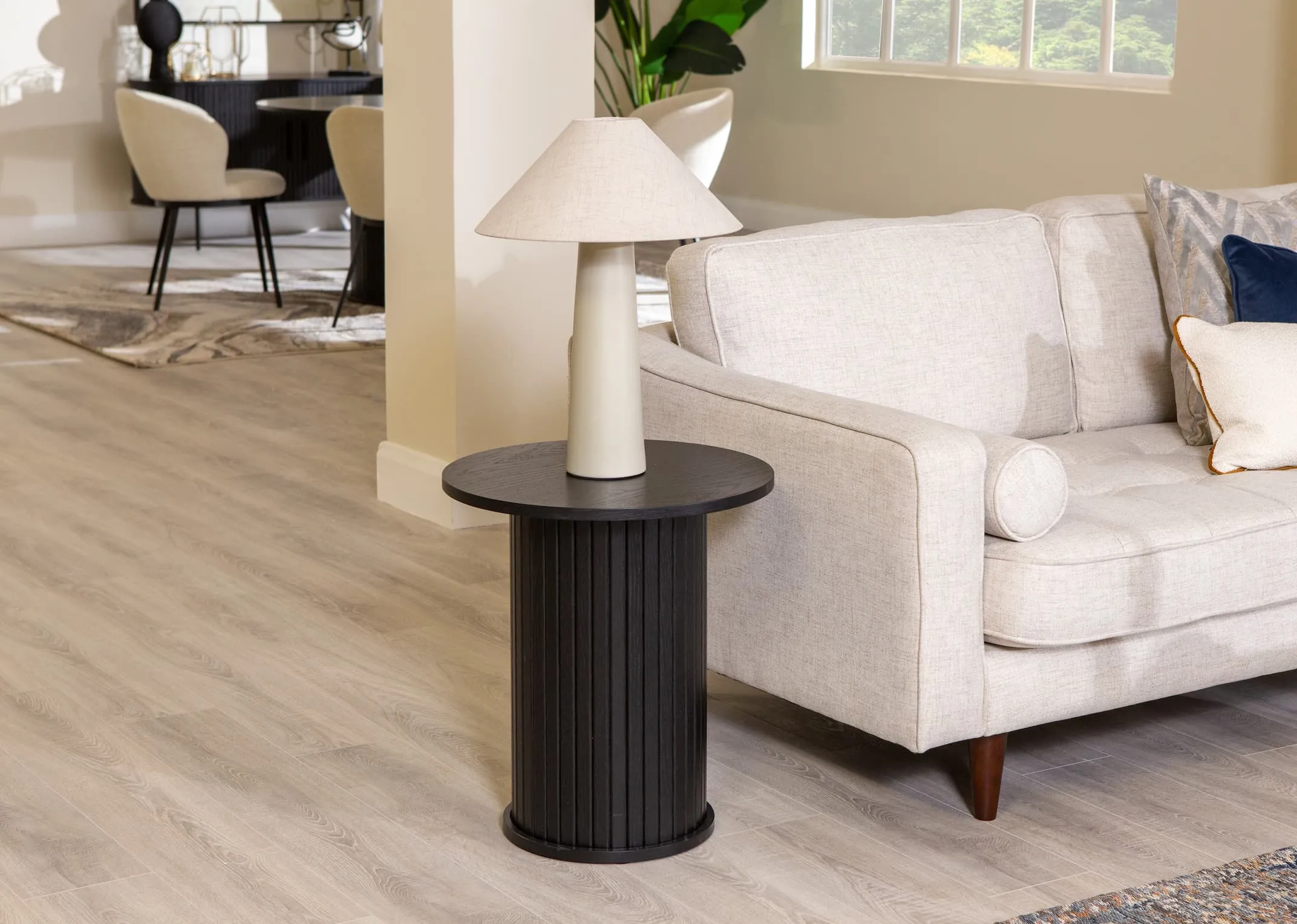 A lifestyle image of the Nola black oak lamp table with Daisy lamp with Genoa sofa