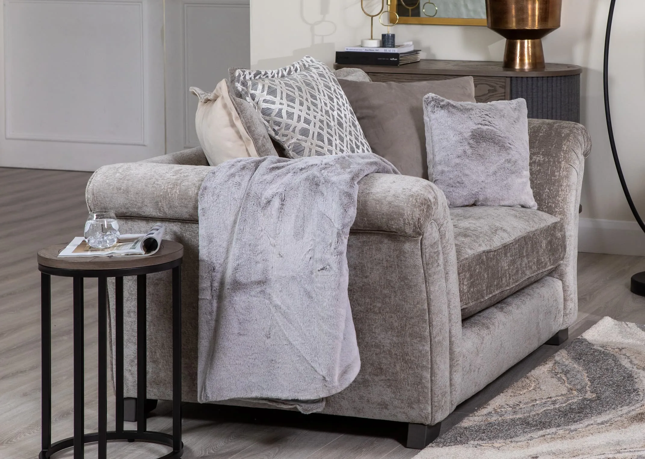 A lifestyle image of the Tabitha Snuggler with Tipped silver cushion and matching throw with Monrie side table.