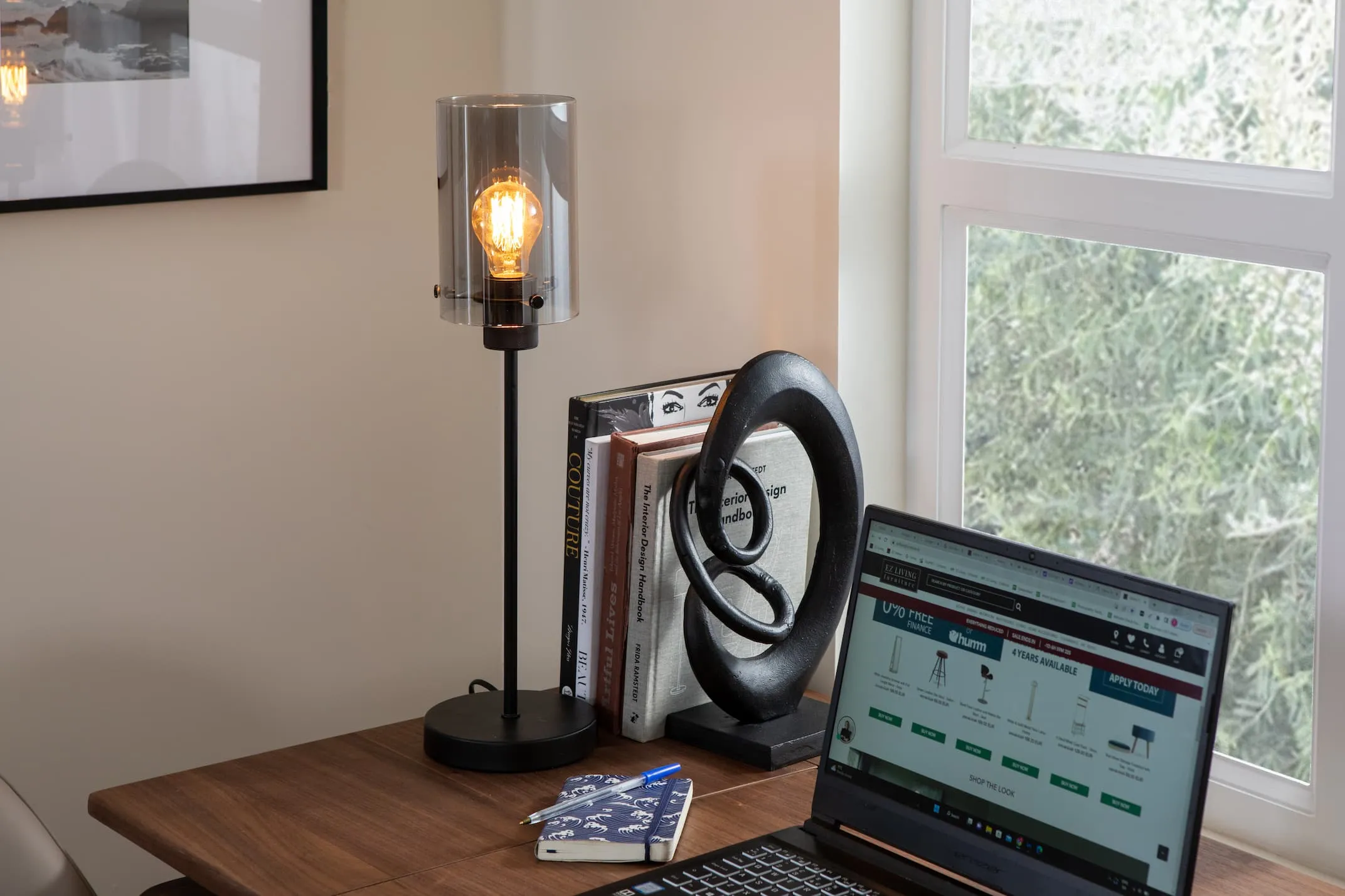 A lifestyle image of the Karina black lamp switched on with the Orbit desk with laptop