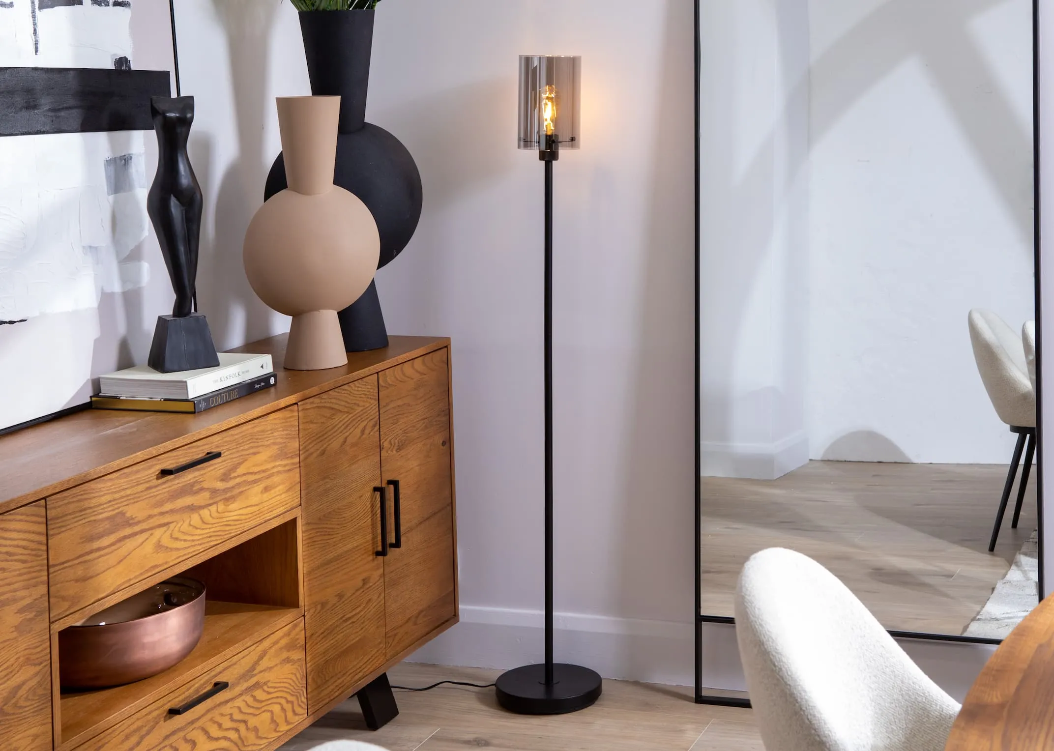 A lifestyle image of the Leanne smoked glass floor lamp with the light on paired with Oslo sideboard.