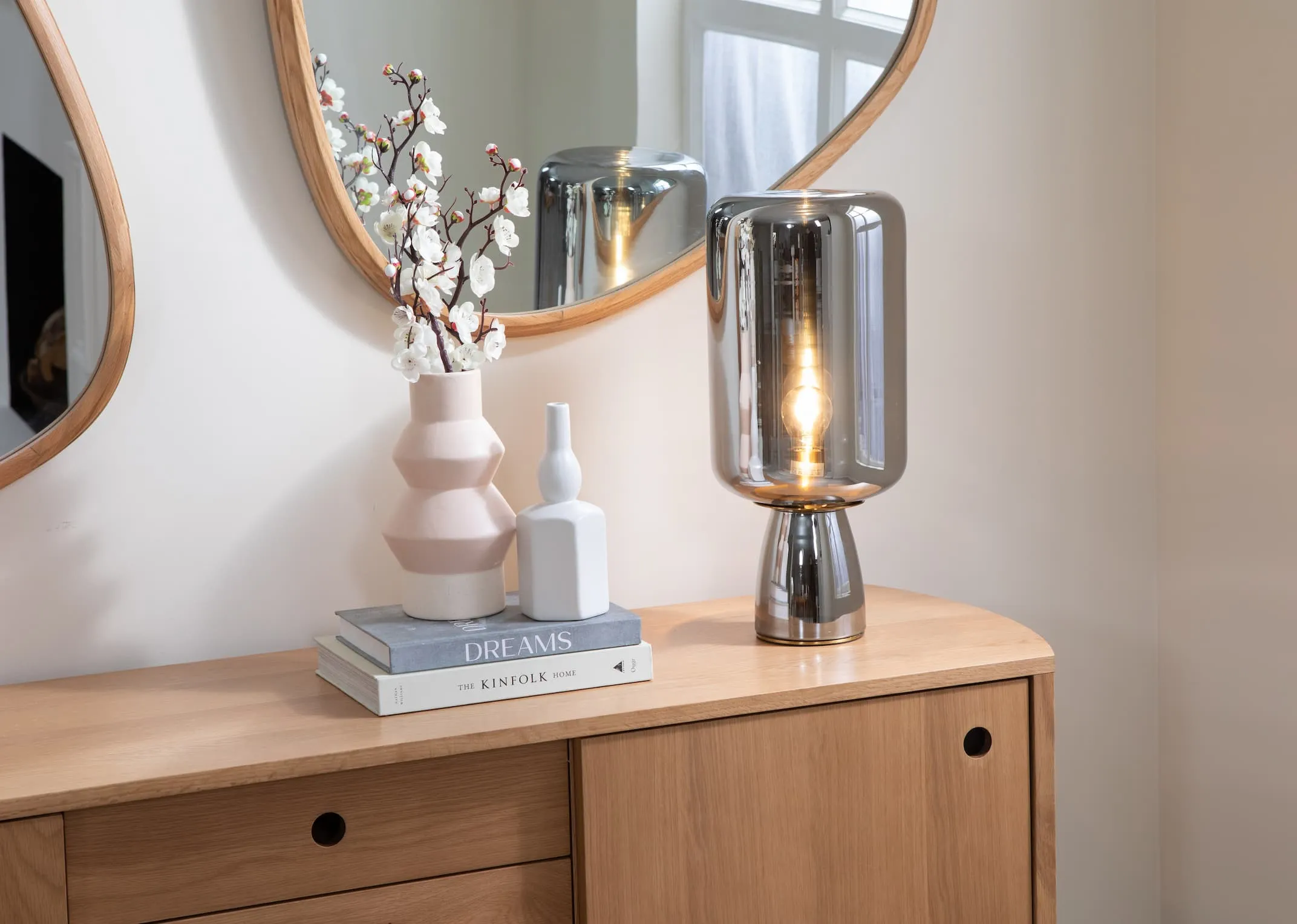 A lifestyle image of the Lotta table lamp switched on with the Copenhagen sideboard and Cody mirror.
