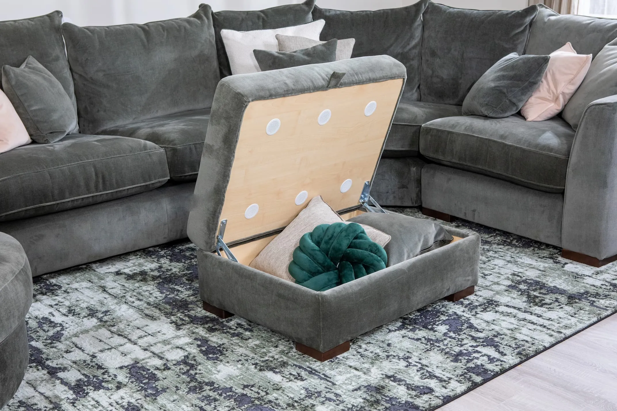 A lifetsyle image of the Lucius green footstool open to show storage for cushions and throws etc with corner sofa and rima rug.