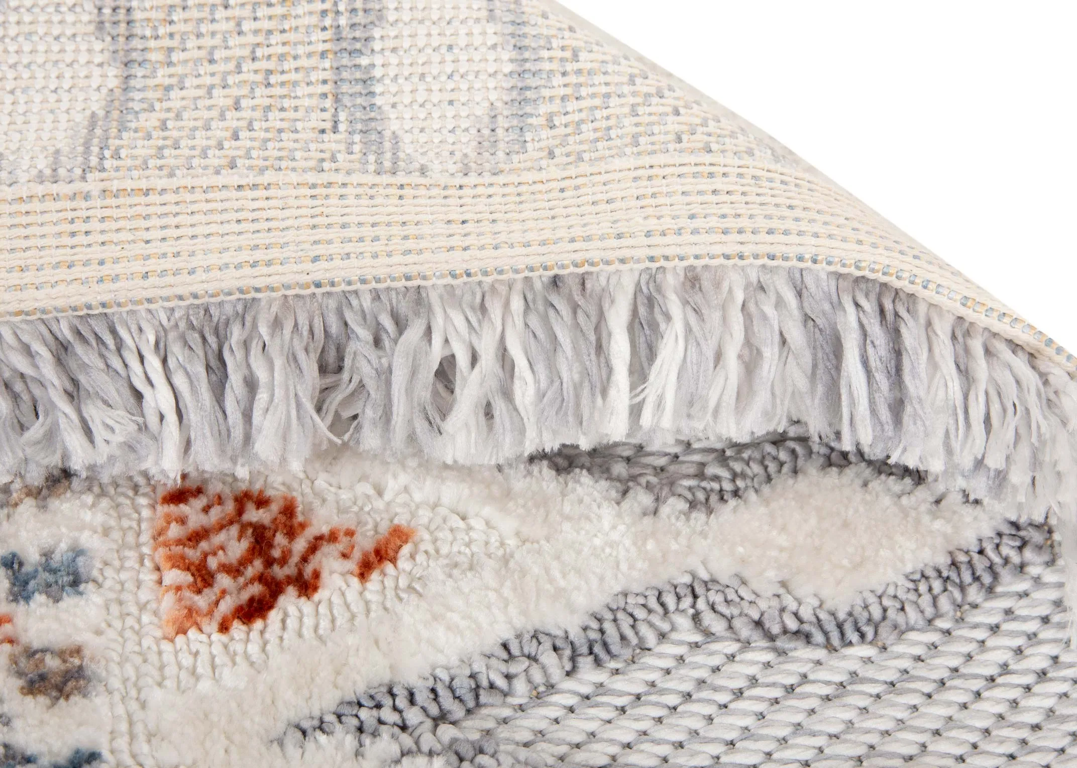 A white medium rug with red gold yellow and blue geometric design from EZ Livings Holiday range. Closeup of fringed trim