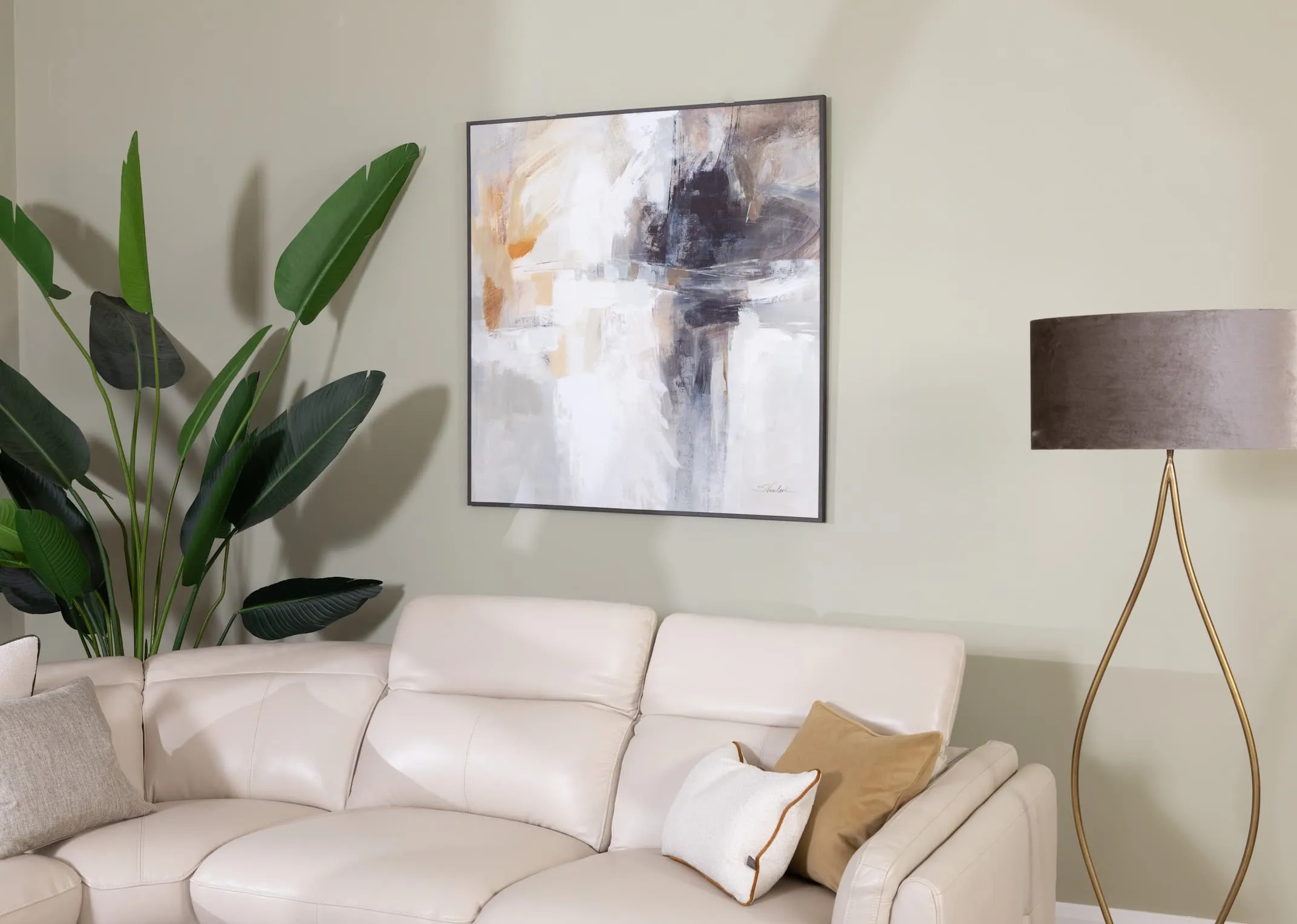 A lifestyle image of the Integrity Canvas with Strellitiza Palnt and Bergamo sofa with cream & gold cushions