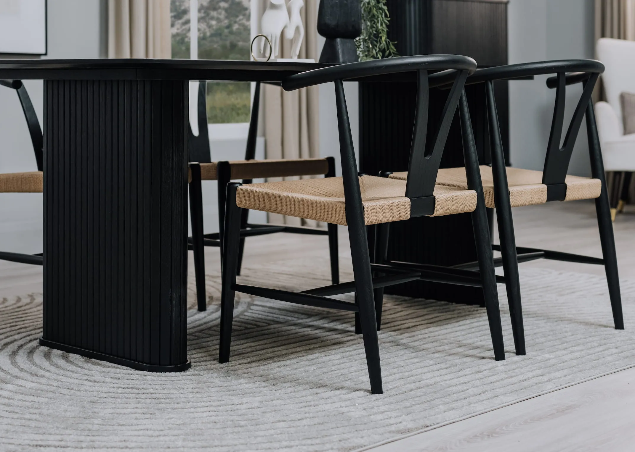 A lifestyle image of the Nola black dining table with cape dining chairs with woven seat on the Eli rug.