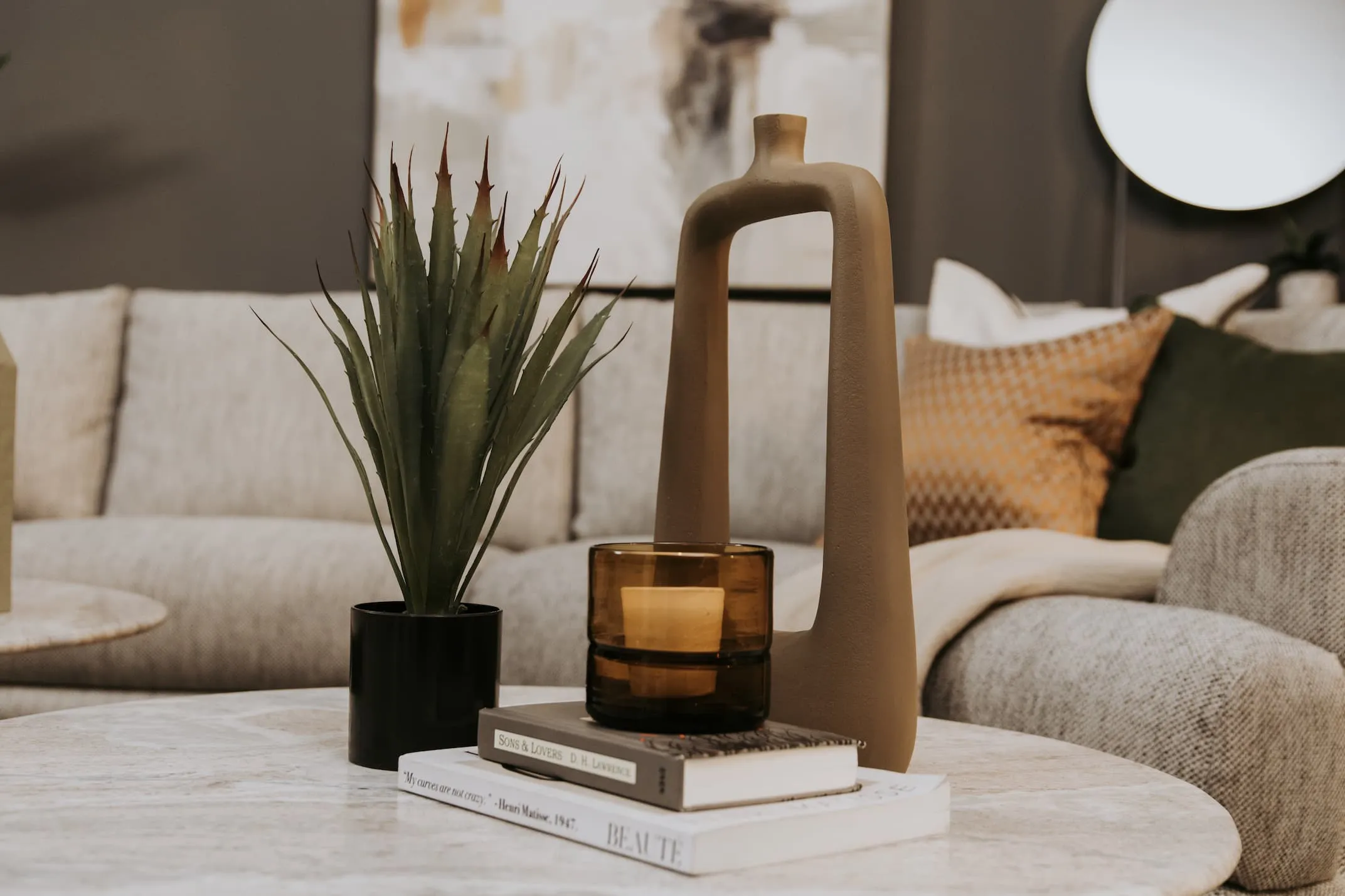 A lifestyle image of the Light Brown vase with artificial plant on a coffee table with candle holder.
