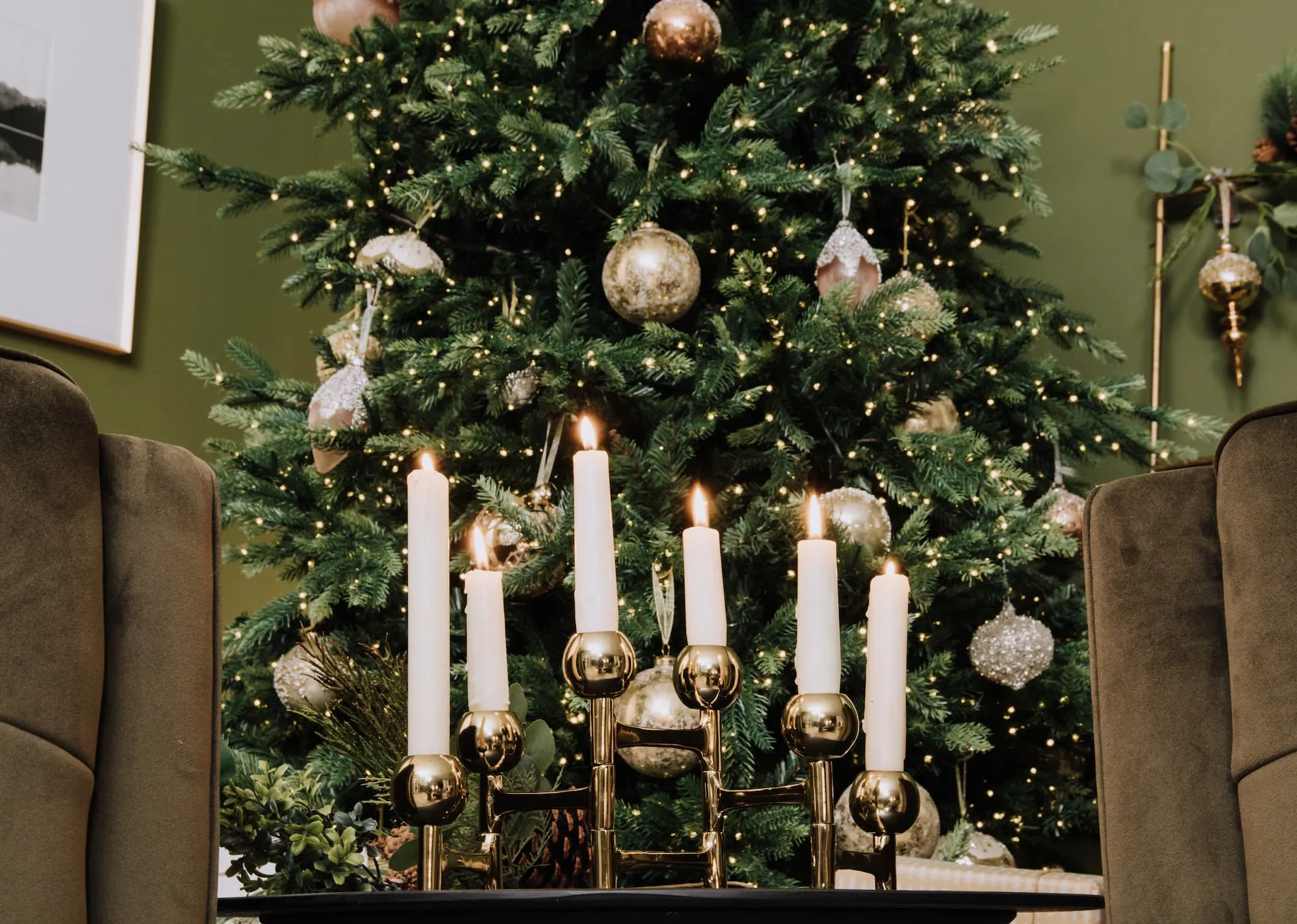 A lifestyle image of the Rockefeller tree with the gold folding candle holder below it with candles lit.