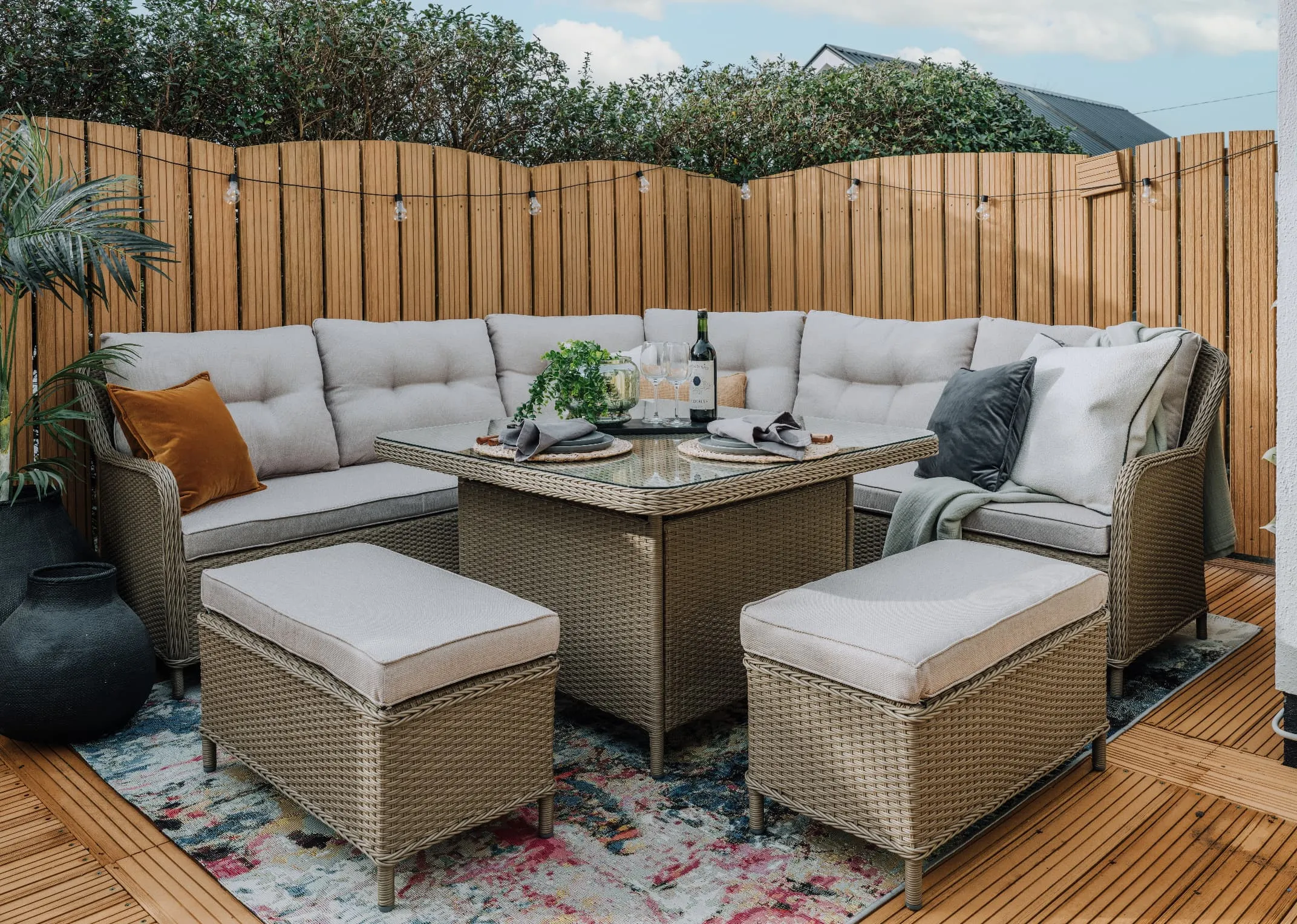 A lifestyle image of the Marbella corner garden set in a backgarden with Luxor rug and a selection of cushions.