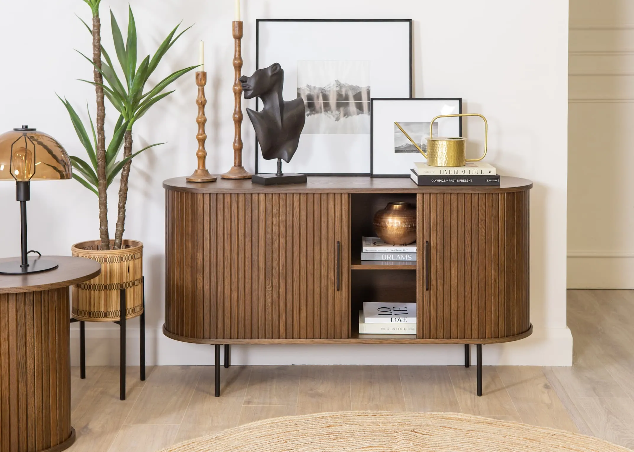 A lifestyle image of the Nola smoked oak sideboard opened with books and vases inside and Face bust and Arabel frames