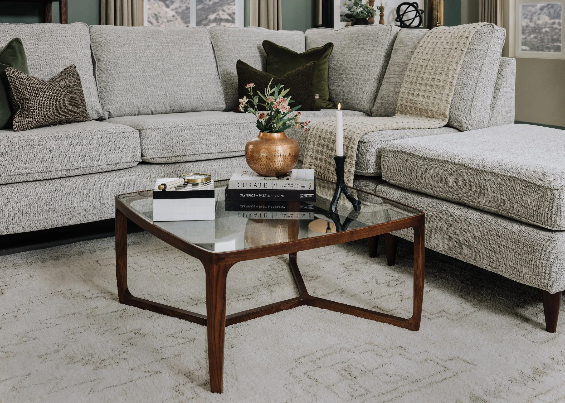 A lifestyle image of the Bella sofa with Cameo glass coffee table with vase and books and candleholder.