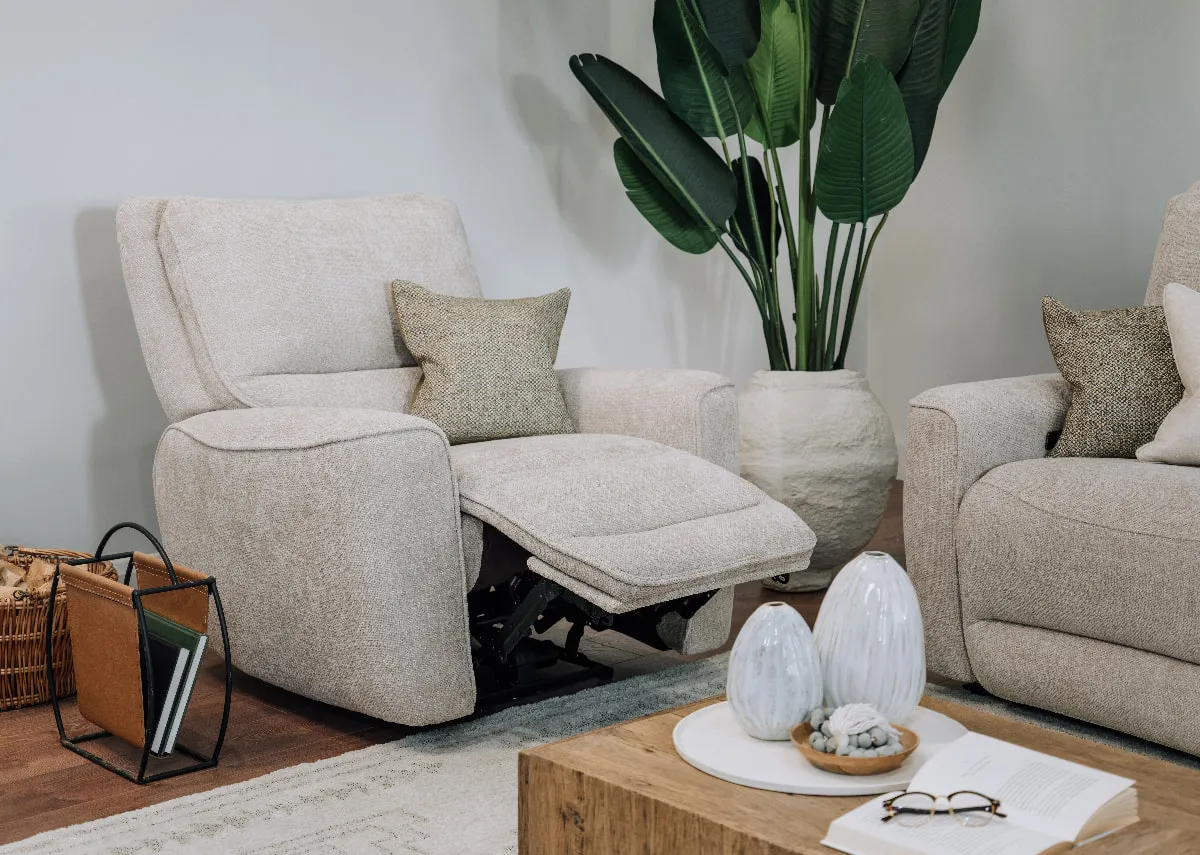 A lifestyle image of the Ashbrook Power recliner in recline mode with nova coffee table and a plant.