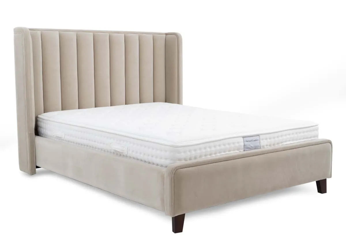 A beige fabric bedframe with high winged headboard from EZ Liings Lowe range. Angled view of walnut feet.