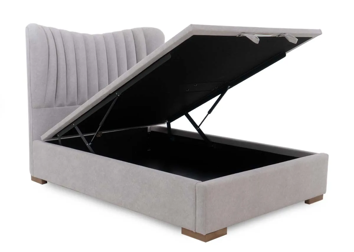 A light grey fabric ottoman bed with its spacious storage compartment open revealing the black interior. It has a vertically tufted headboard.