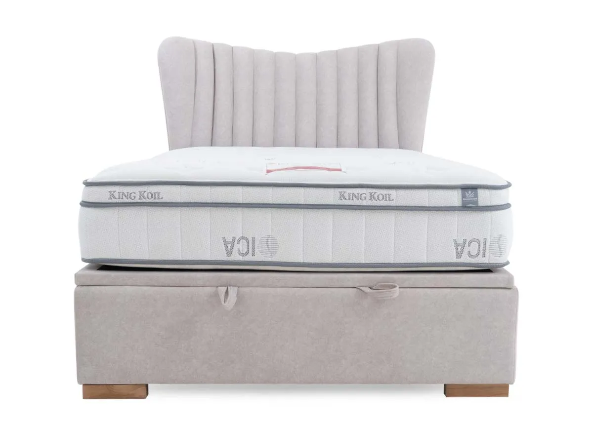A light grey fabric ottoman bed with a white mattress on top featuring a vertically tufted headboard and a discreet handle on the bed base.