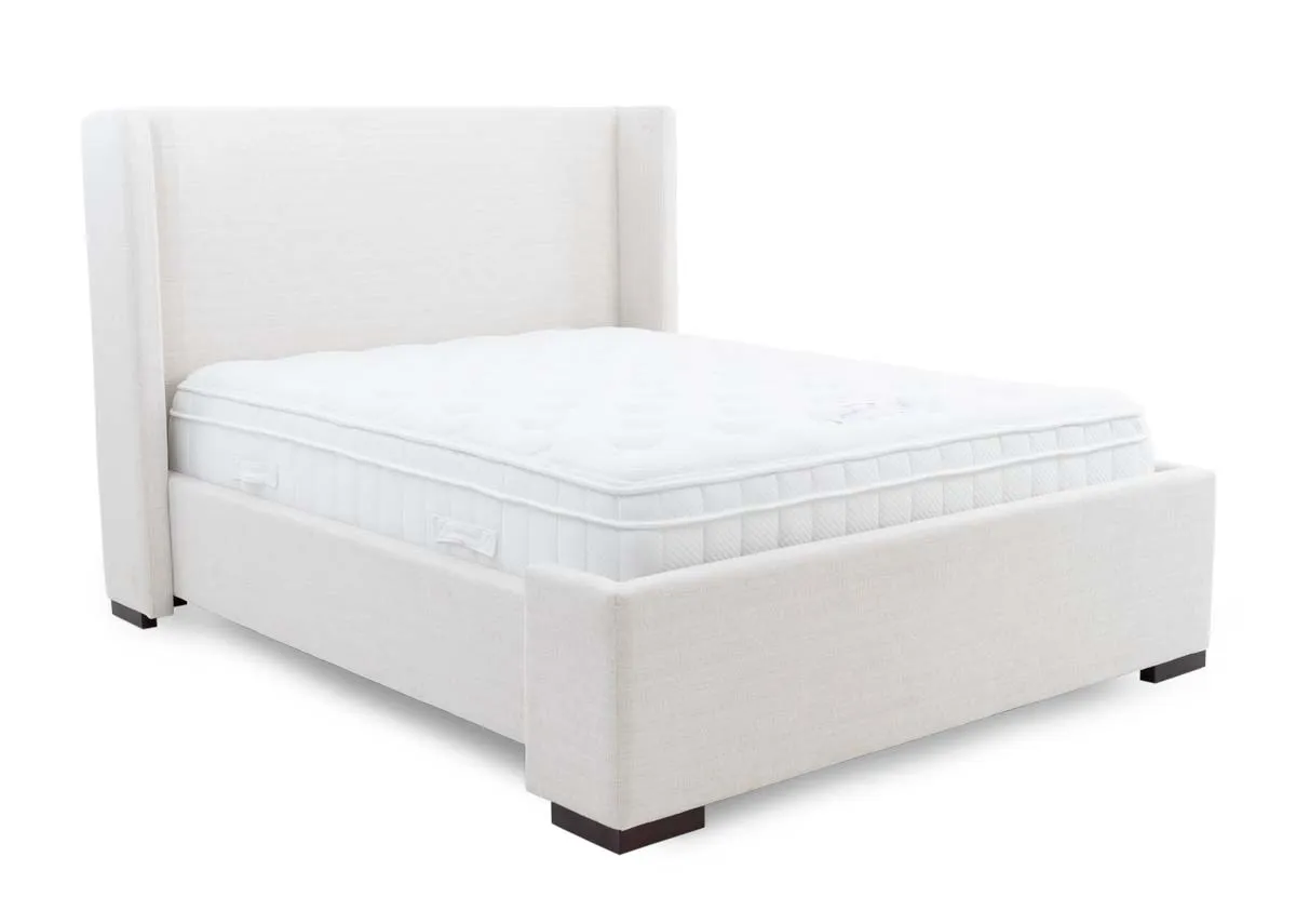 A beige fabric bed frame with high winged headboard from EZ Livings Quay west range. Angled view of bed with mattress not included