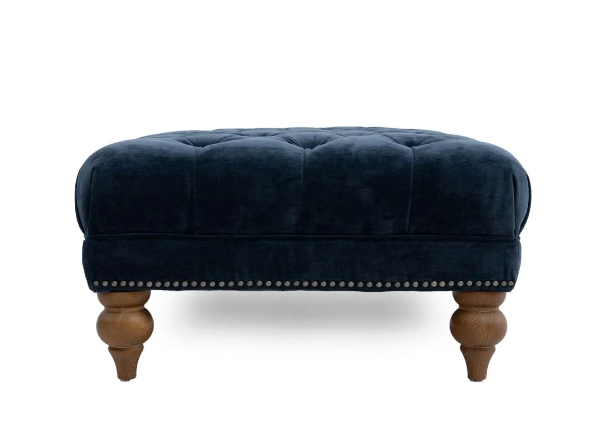 A blue fabric rectangular footstool from EZ Livings Adare range. Side view of stud trim and ash feet