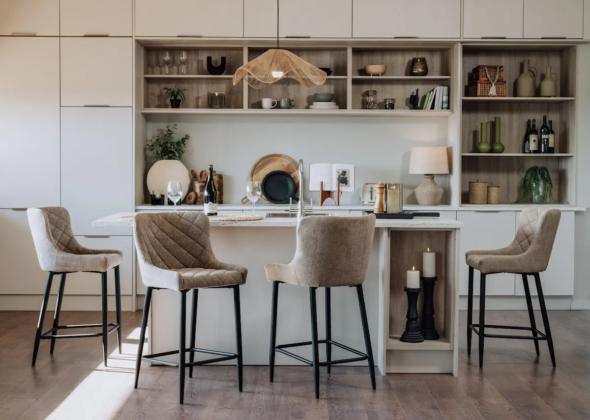 A lifestyle image of four Ottowa Bar Stools in taupe paired with a cream kitchen island in a neutral kitchen setting.