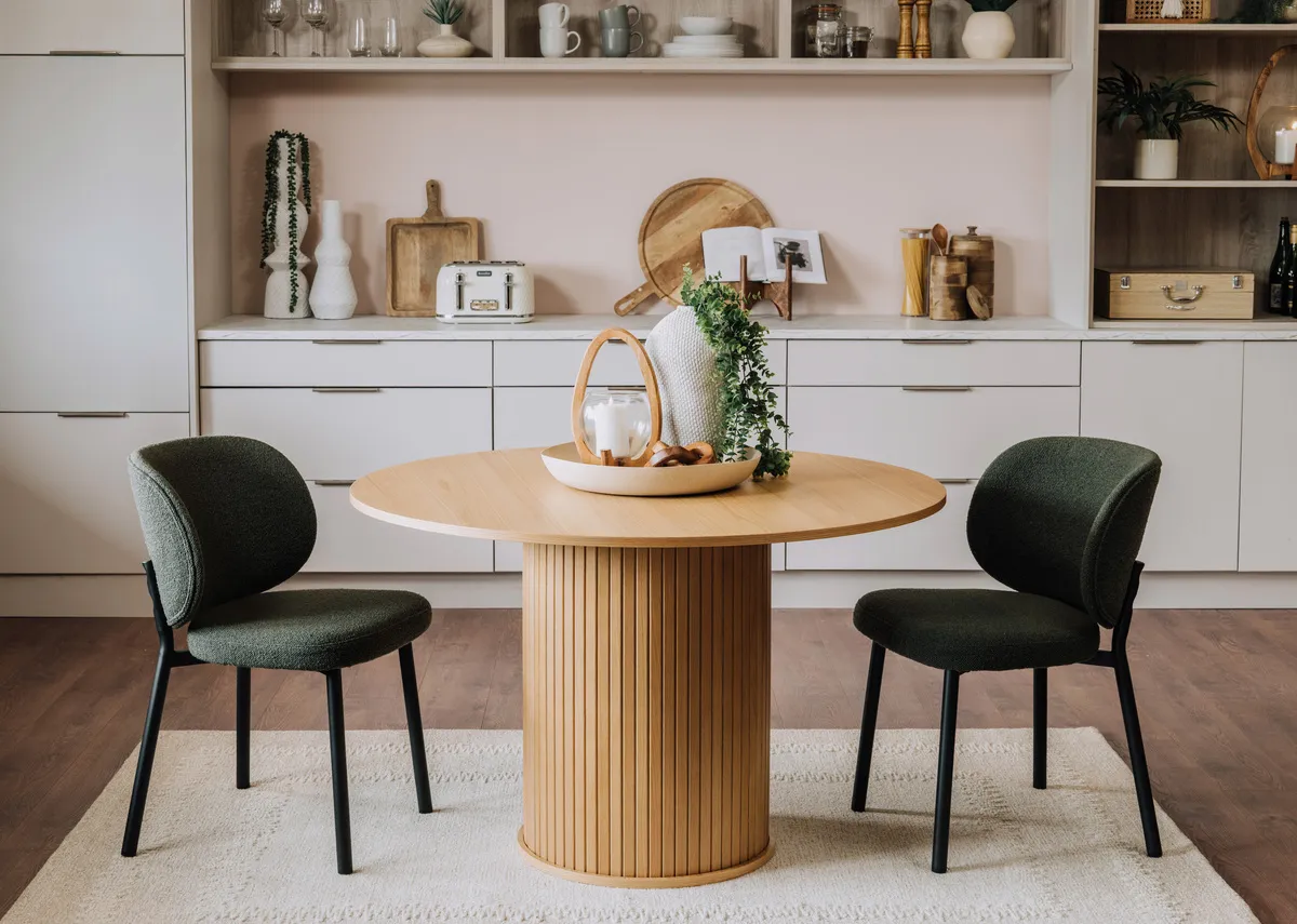 A lifestyle image of the Sovata rug with Nola round oak dining table and 2 green swan chairs