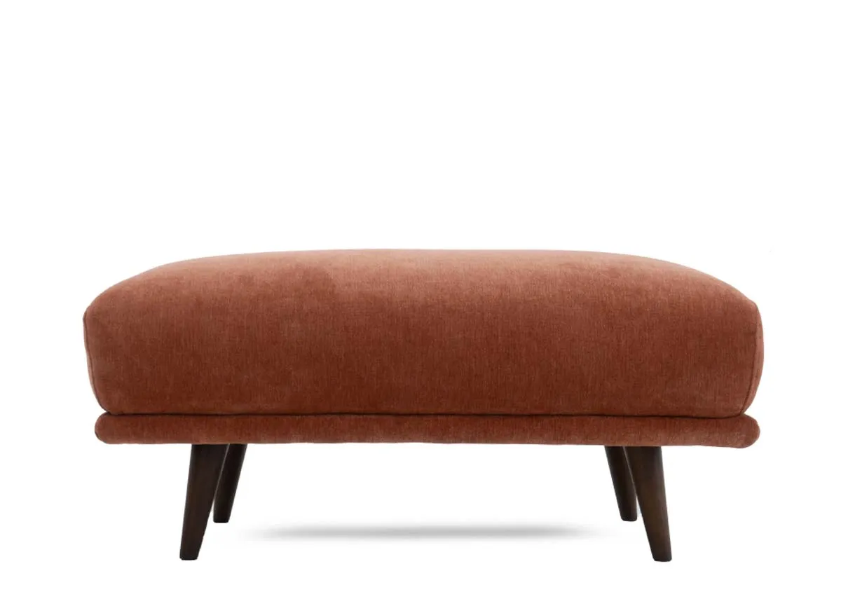Large footstool in rust colored fabric presented from a straight on front view.