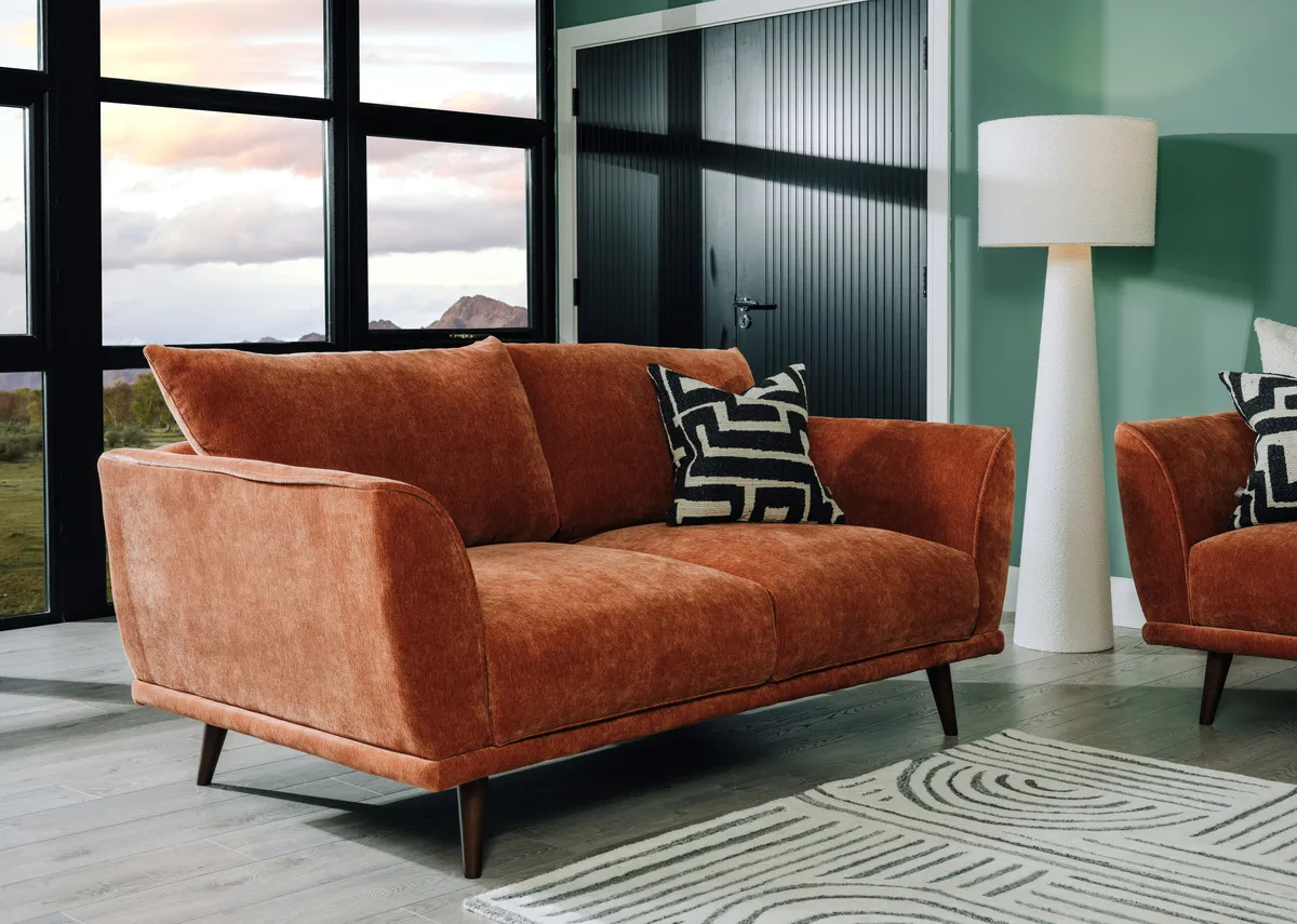 A lifestyle image of the Boutique rust sofa with geometric cushion and White floor lamp