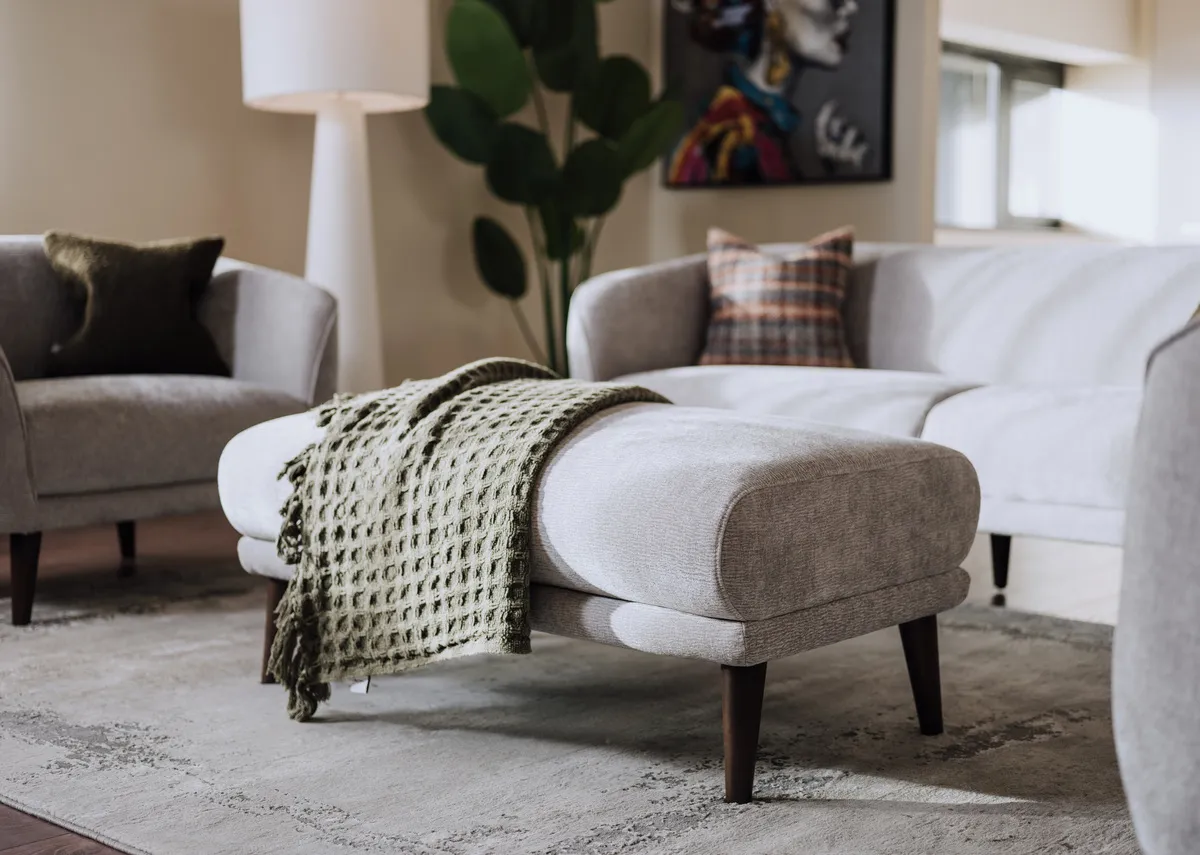 A lifestyle image of the Amber footstool with a green nthrow with the Tolka lamp in background.