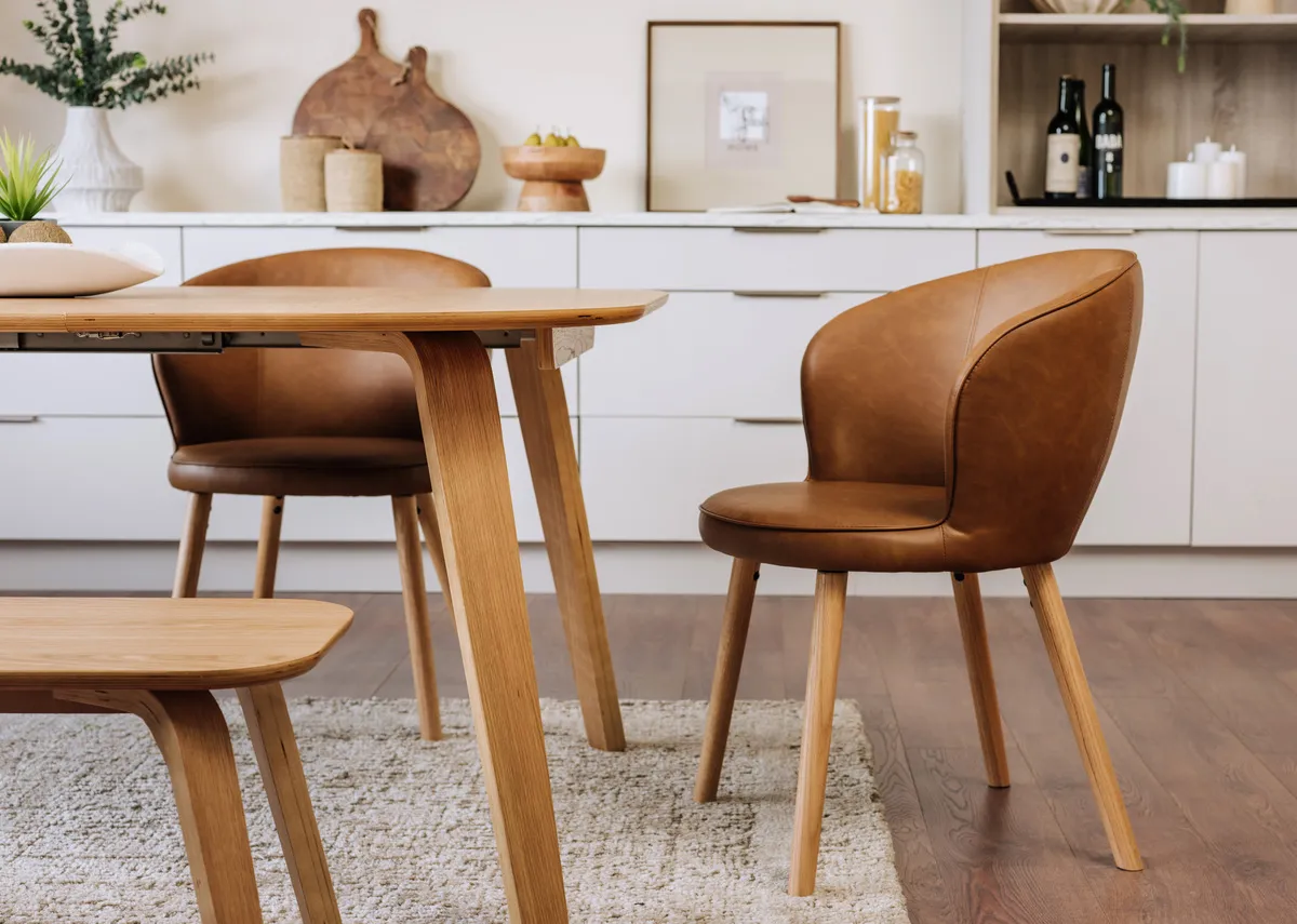 A lifestyle image of the Gain carver chair with oak legs paired with the Anton dining table.