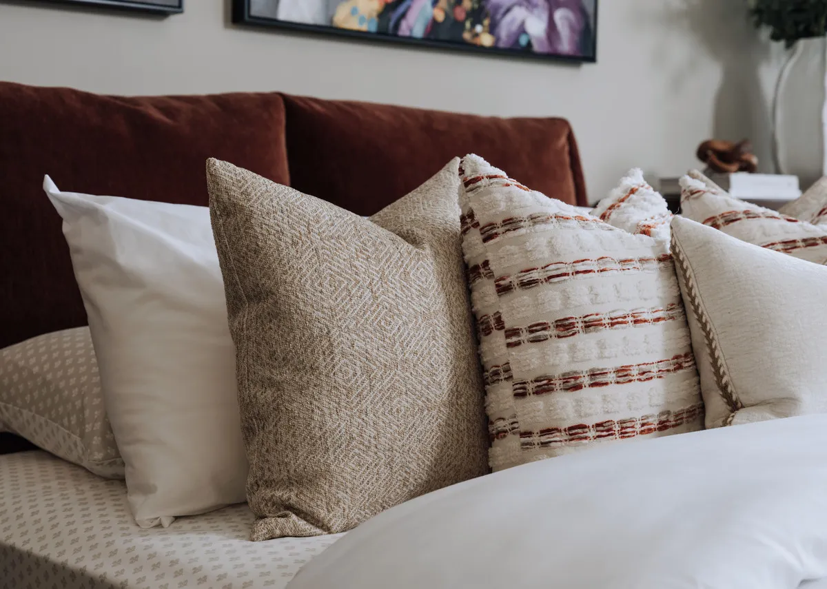 A lifestyle image of the Warm harvest cushion with a selection of cushions oin nthe Comfy rust bedframe.