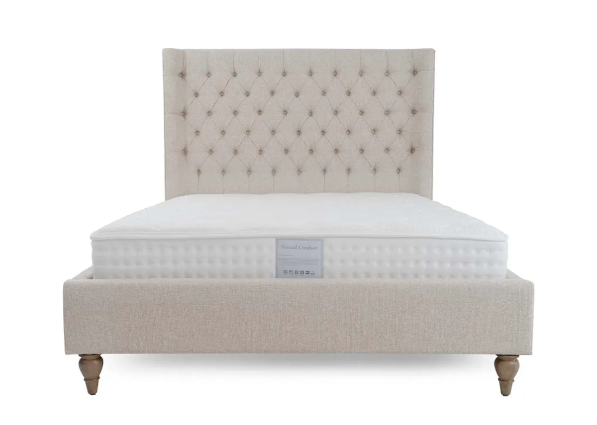 A cream fabric bed frame from EZ Livings Chelsea range. Front view of tufted button headboard with winged sides.