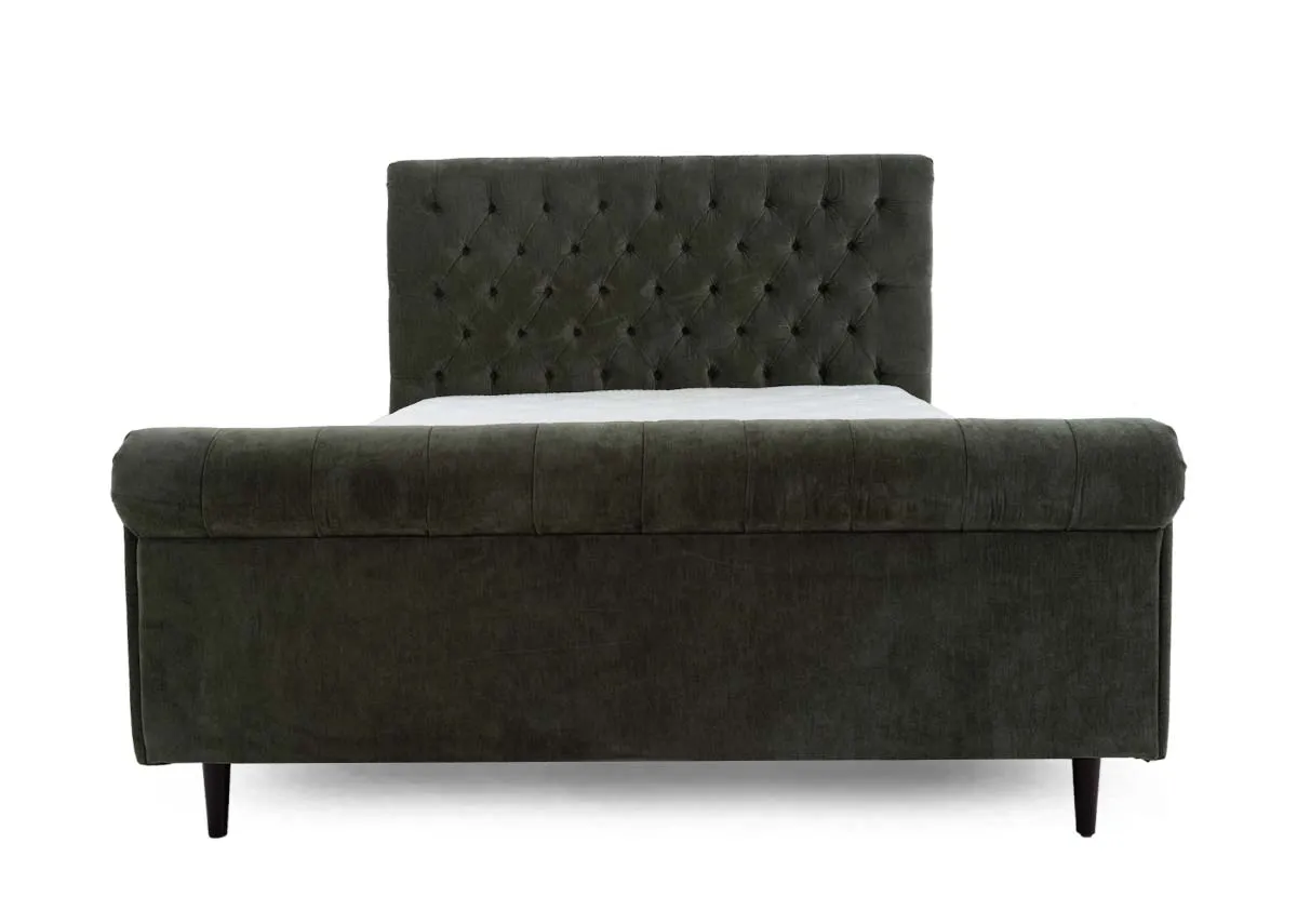 A green fabric bedframe with tufted Chesterfield detail and scrolled finish head and footboard. Front view of detail on footboard