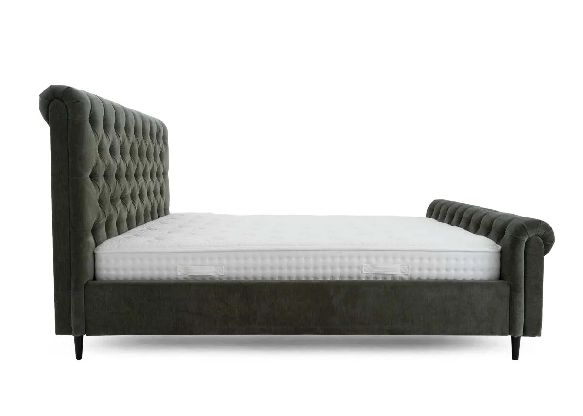 A green fabric bedframe with tufted Chesterfield detail and scrolled finish head and footboard. Side view of bed with mattress not included.