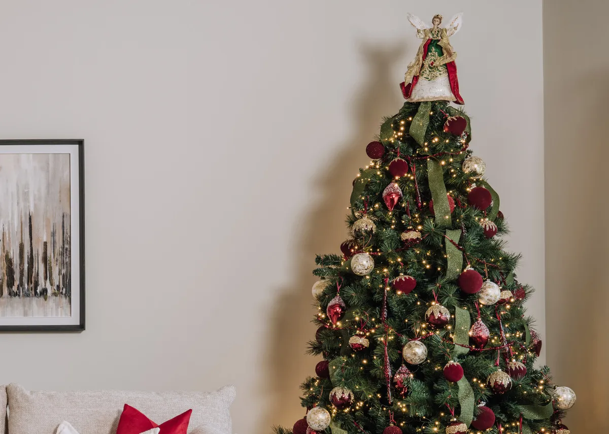 A lifestyle image of the Angel topper with a selection of red and gold baubles on a sherwood christmas tree