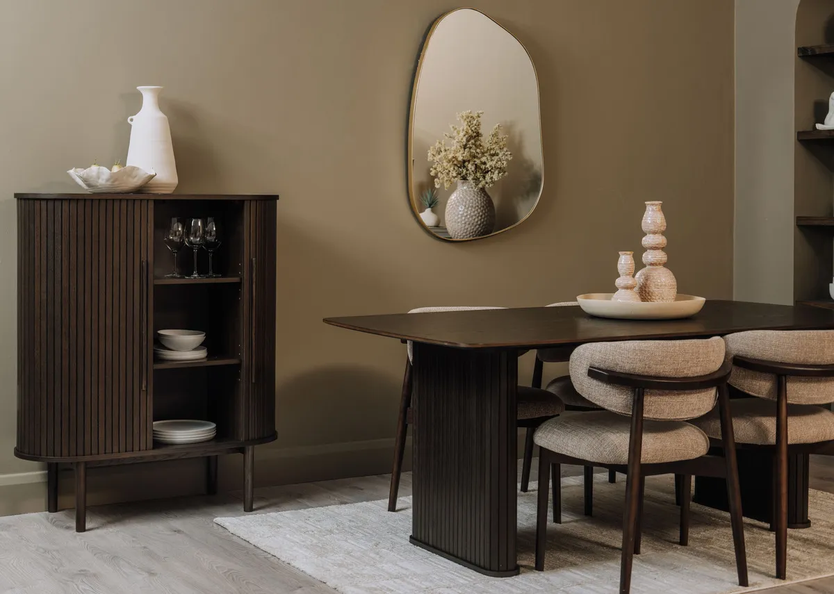 A lifestyle image of the Nola Cabinet with doors open showing space for dinnerware and glasses with the matching dining table and Delfina mirror