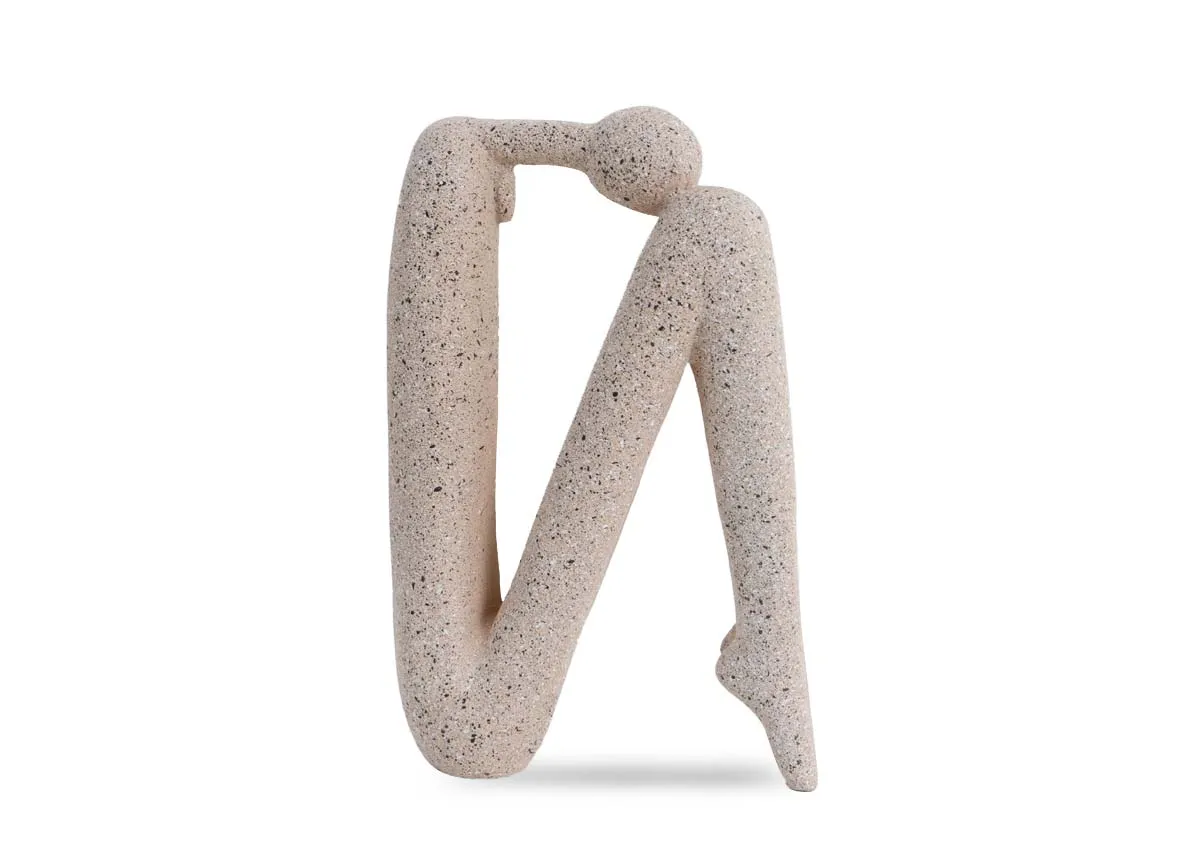 A beige stone human ornament of a head resting on knees pose.Side view