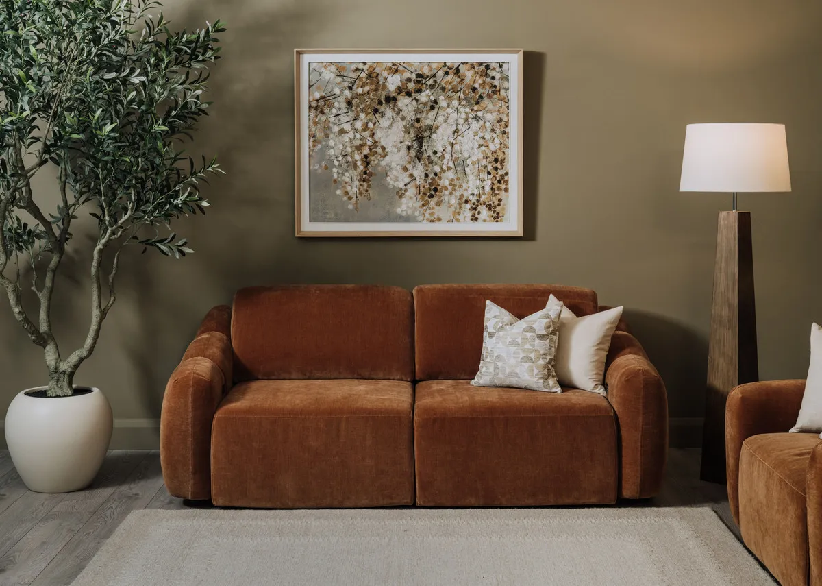 A lifestyle image of the Eleanor rust 2 seater as a fixed sofa with Bliss painting and Eleanor armchair.