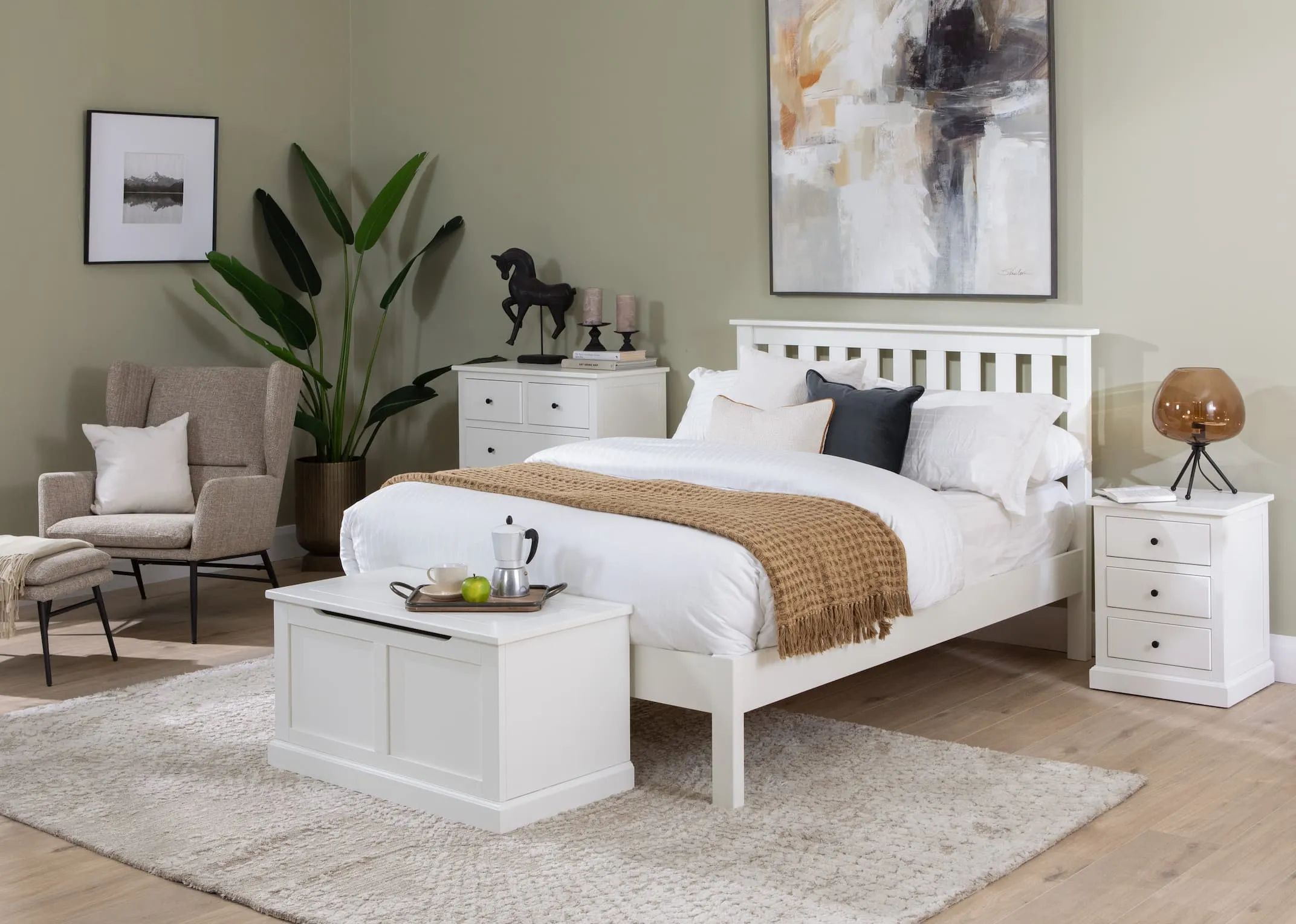 A lifestyle image of the White Atlas bedroom range including bedframe & chest of drawers & locker & blanket box with Boston armchair & footstool set