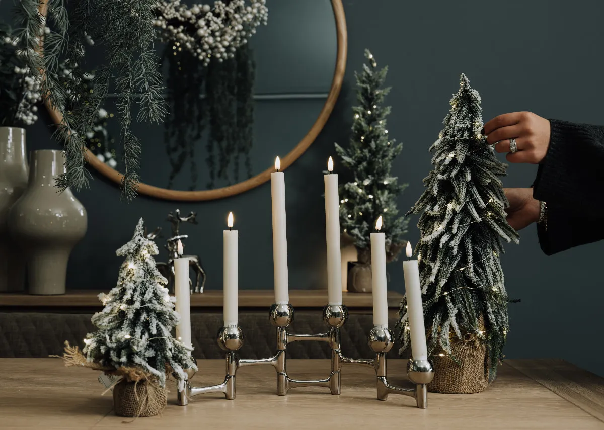 A lifestyle image of the Folding candle holder in silver with Eve snow trees on a dining table.