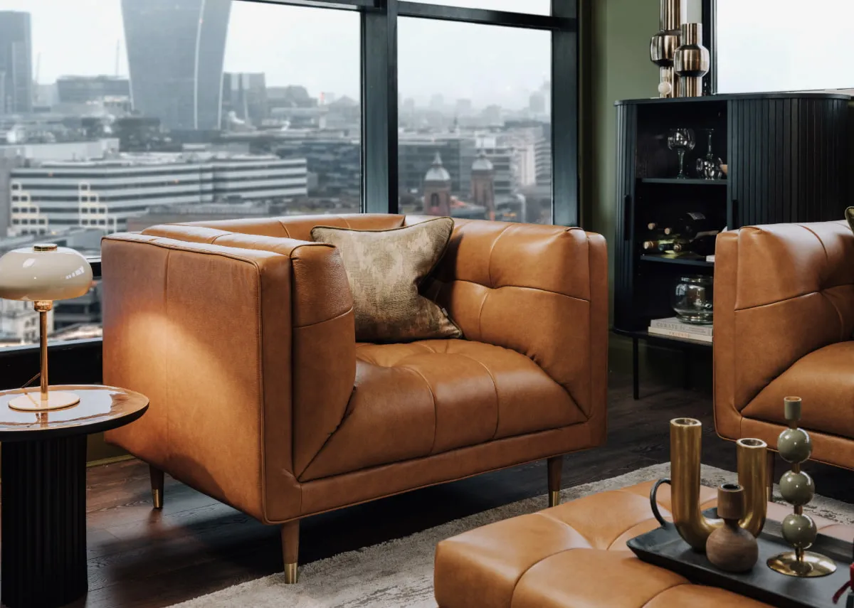 A lifestyle image of the Grace tan leather armchair with a cityscape view with Nola black cabinet.