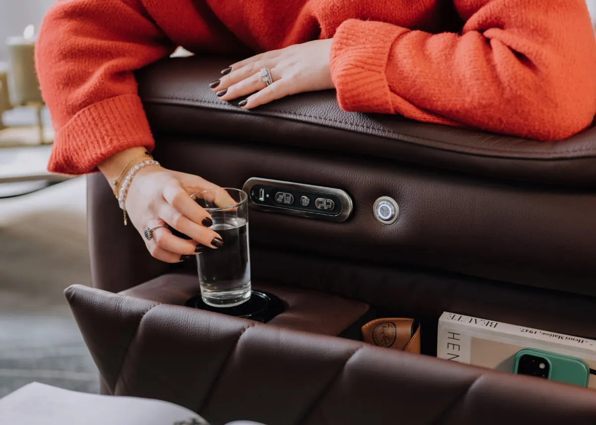A closeup lifetsyle image of Ola placing a glass of water in the hidden cup holder under armrest