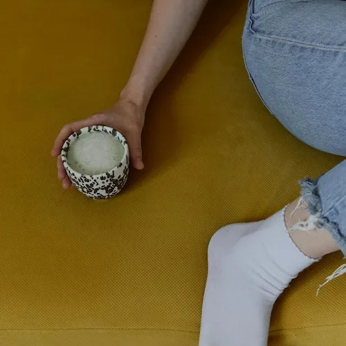 Woman sitting on mustard-coloured couch with matcha latte 