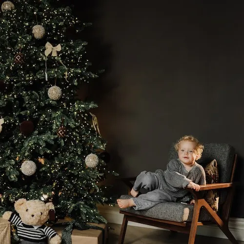 Decorated Christmas tree with child sitting on a chair next to it.